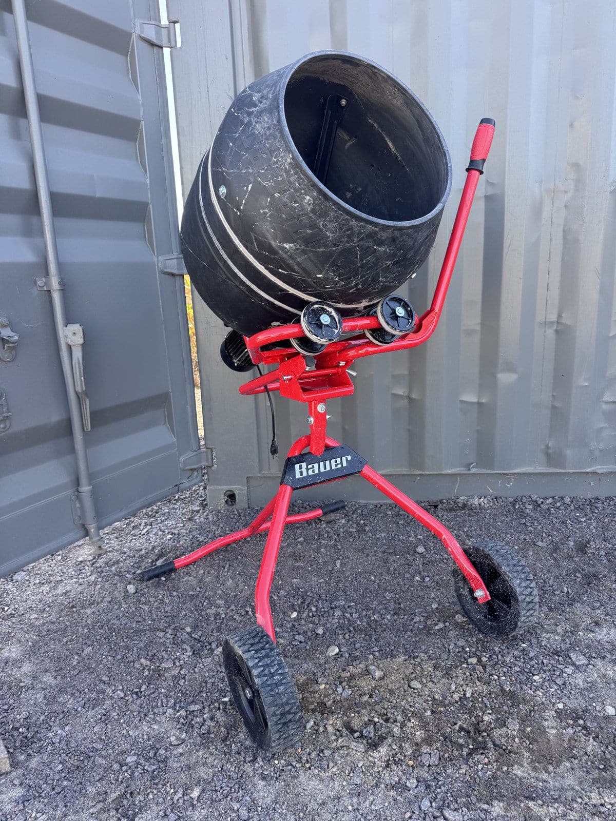 Red Bauer electric cement mixer with a black poly drum, parked on gravel
