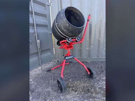 Red Bauer electric cement mixer with a black poly drum, parked on gravel
