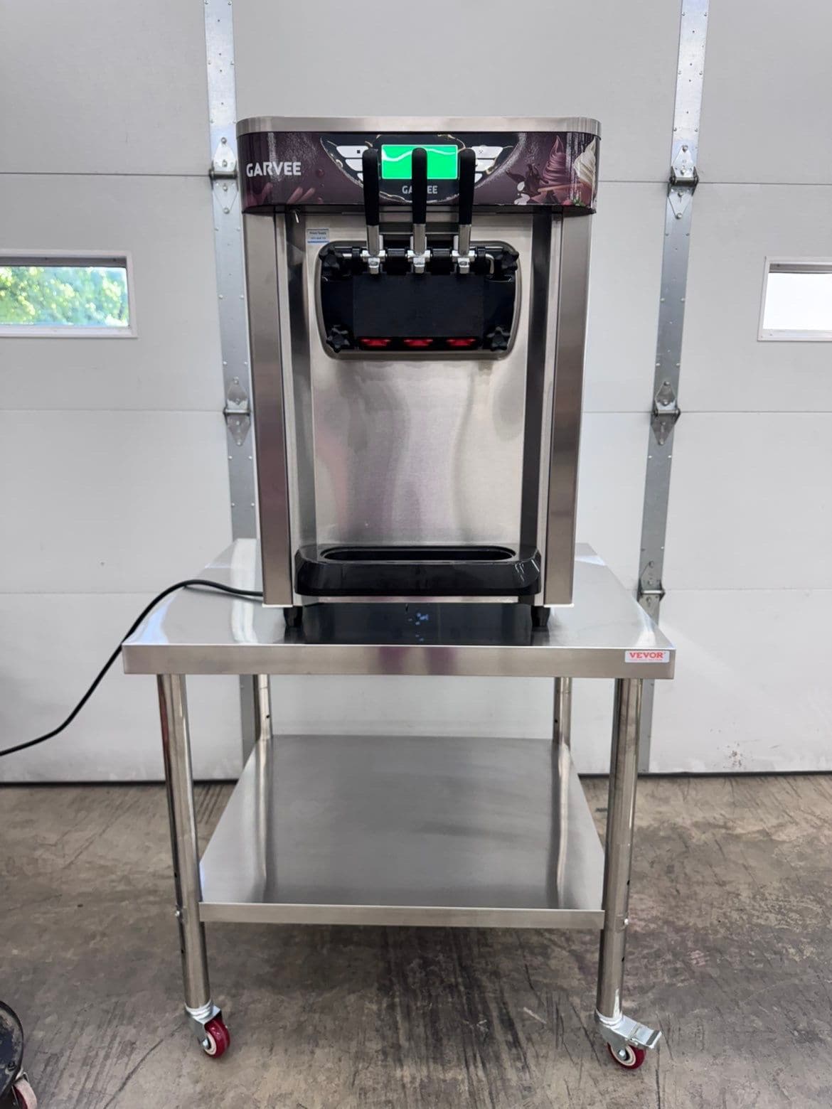 Countertop soft-serve ice cream machine with three dispensing handles, shown on a stainless steel stand