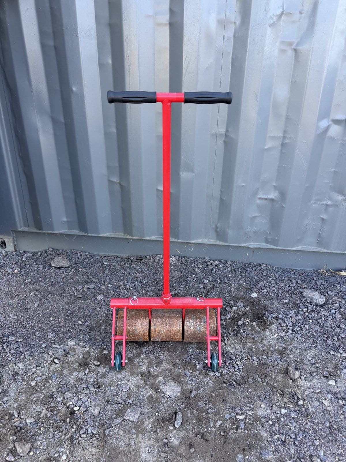 Red three-section steel floor roller with a T-handle, standing on gravel