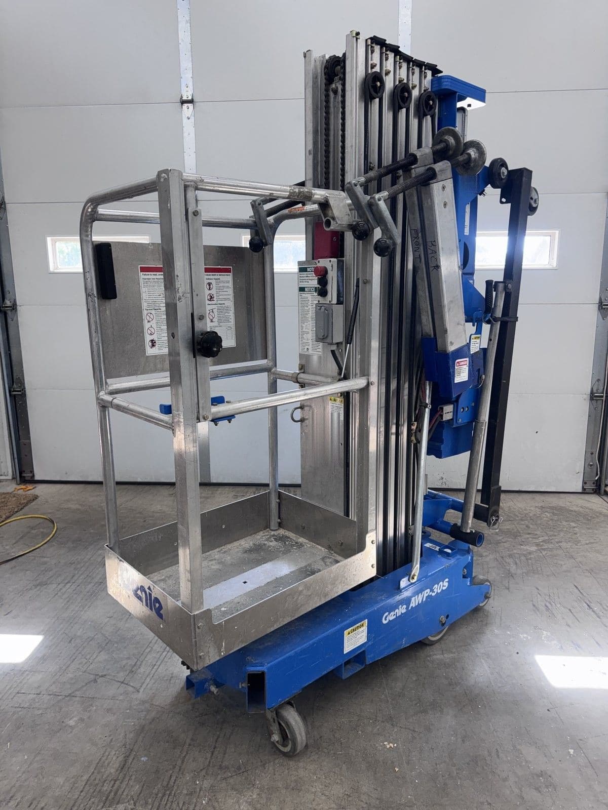 Blue Genie AWP-30S push-around personnel lift with its platform lowered, parked in a shop