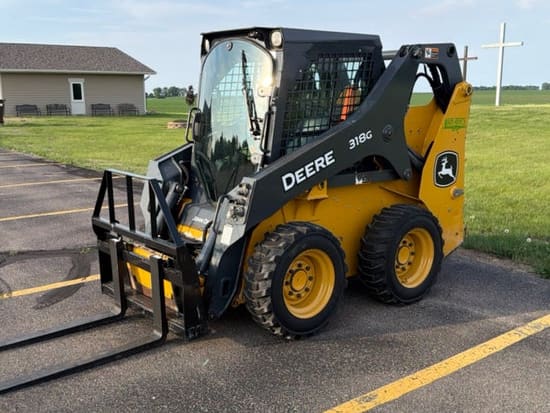 John Deere 318G skid steer with pallet forks, parked on pavement