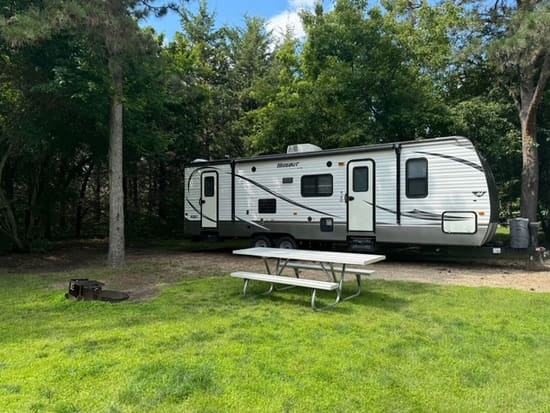 Keystone Hideout travel trailer parked under trees beside a picnic table