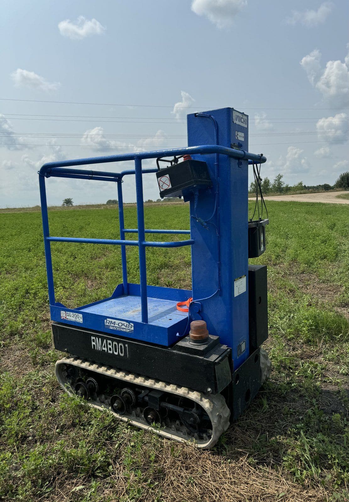 Blue tracked personal manlift with its platform lowered, parked on grass
