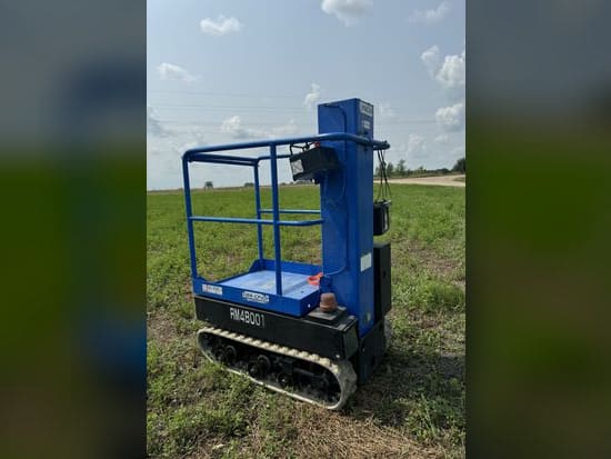 Blue tracked personal manlift with its platform lowered, parked on grass
