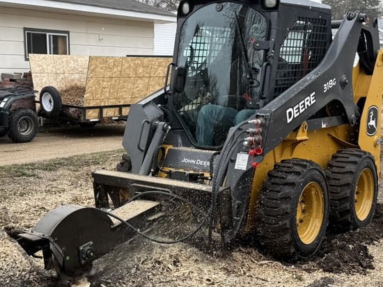 Hydraulic stump grinder attachment on a John Deere skid steer, grinding down a stump