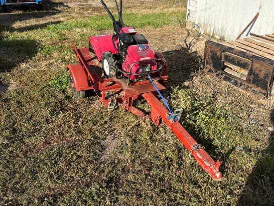 Red Honda tiller with its tilt trailer on a grassy yard