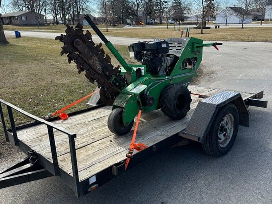 Green Vermeer RTX130 trencher strapped onto a utility trailer